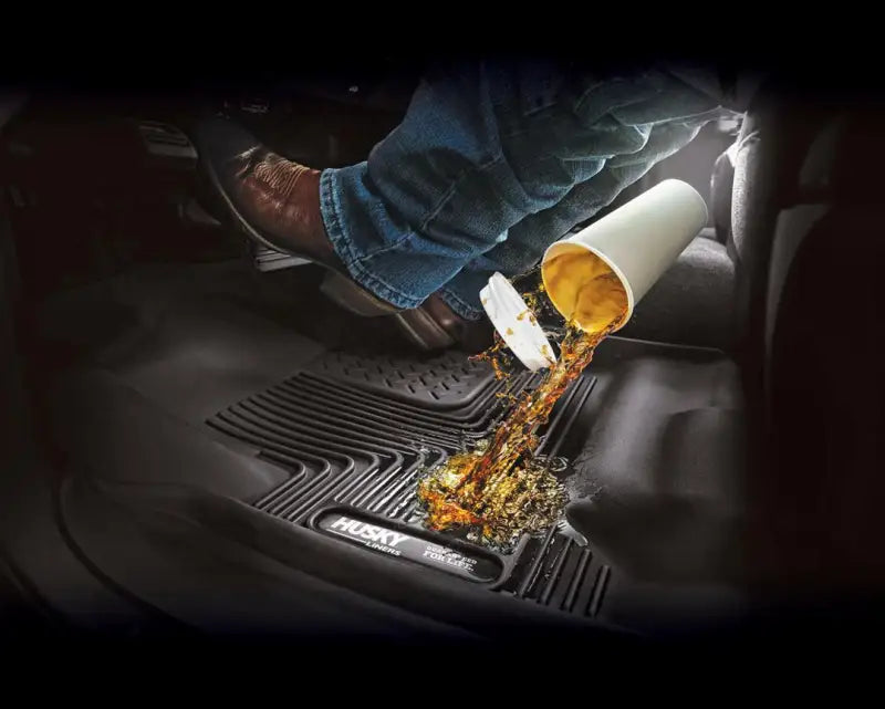 Husky Liners X-act Contour floor liner in black with raised edges and channels resisting a coffee spill from a tipped cup.