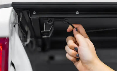 Person’s hand operating access lomax tri-fold cover latch on Ram 1500 truck bed