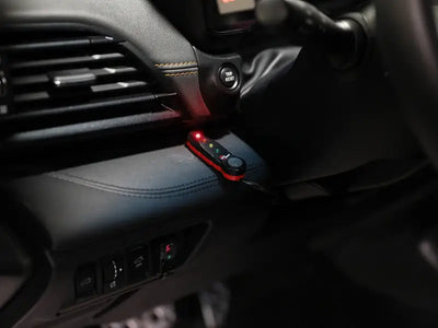 A compact, red and black electronic device with indicator lights, possibly for a vehicle’s dashboard.