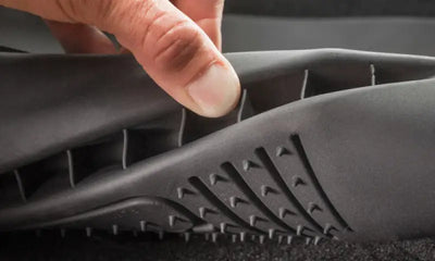 Hand holding and bending a black Husky Liners® molded floor liner made of thermoplastic elastomer with raised ridges and stay-put cleats.