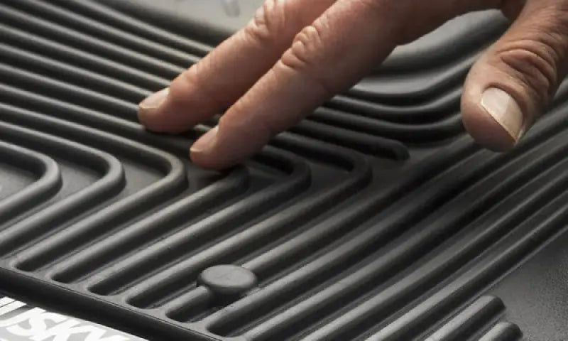 Close-up of a hand touching the textured, raised ridges of a black, molded-fit Husky Liners® X-act Contour® floor liner made from thermoplastic elastomer.