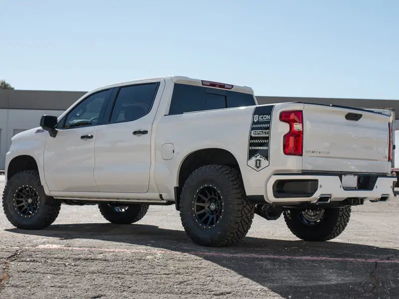 ICON 2019+ GM 1500 1.5-3.5in Stage 2 Suspension System w/Billet UCA installed on a white pickup truck with large off-road tires, parked on a concrete surface.
