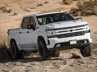 White Chevrolet Silverado 1500 truck off-roading in desert, equipped with ICON 2019+ GM 1500 1.5-3.5in Stage 4 Suspension System featuring billet aluminum upper control arms.
