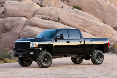 Black pickup truck equipped with K1046DL Fabtech Lift Kit Suspension driving through rugged desert terrain, showcasing enhanced off-road capability and aggressive stance.