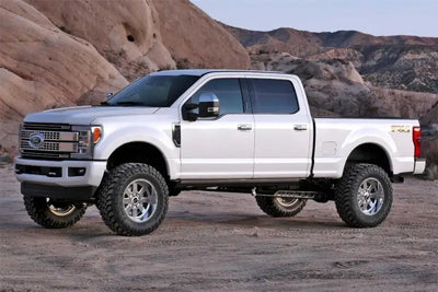 Silver truck equipped with K2218 Fabtech Lift Kit Suspension parked on rugged terrain, showcasing enhanced ground clearance and off-road capabilities. Ideal for RV, automotive, powersports, marine, exterior, and truck accessories. Elevate your ride with Suspension,AVADA - Best Sellers,Must Haves.