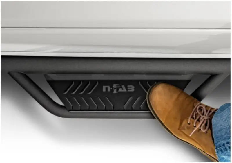 Black stainless steel nerf bar with drop down steps and a tan shoe on it