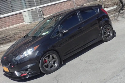 Black mud flap with Rally Armor logo on Ford Fiesta ST with aftermarket wheels and red calipers