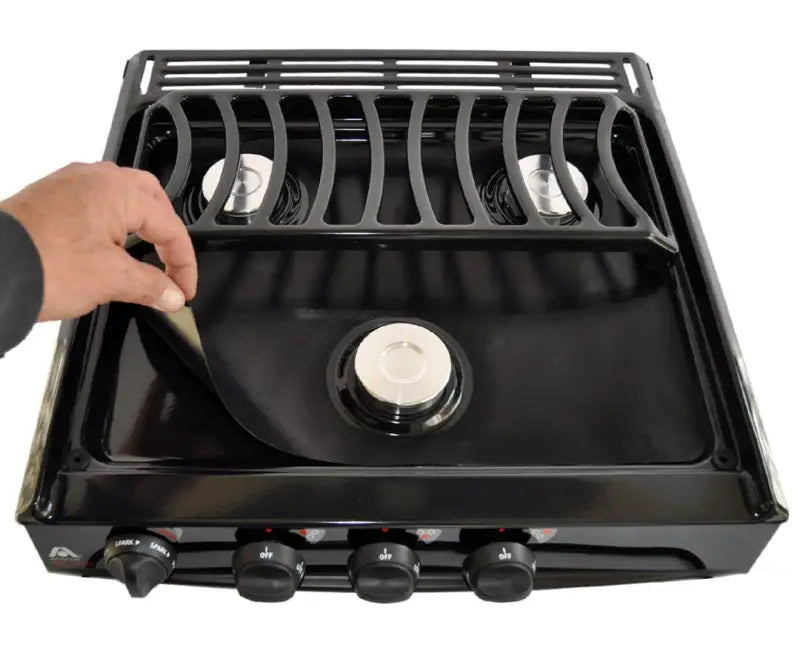 SWRV300 Stove Wrap Stove Top Protectors for Atwood/Dometic stoves, showing a hand lifting the protector to reveal the stove surface underneath.